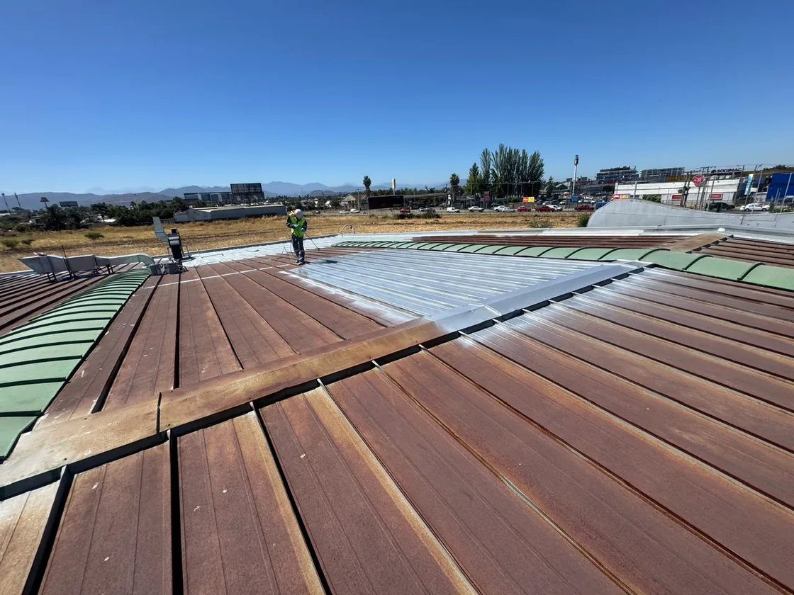 Cubierta metálica industrial oxidada, con un operario aplicando el recubrimiento sobre una sección ya tratada